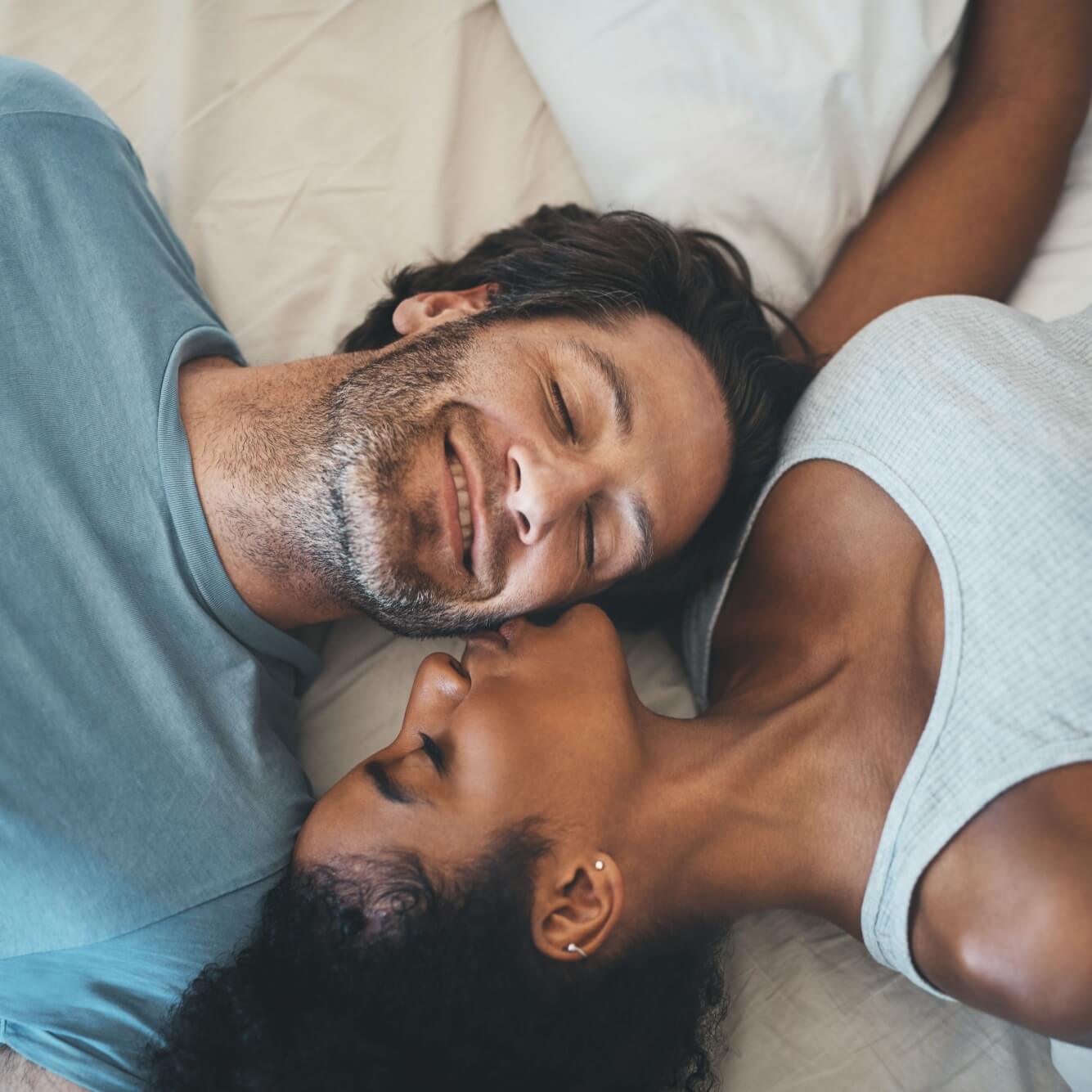 Woman kissing man while lying in bedroom