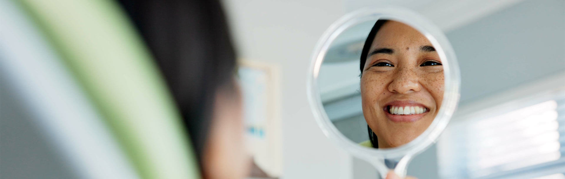 happy woman with mirror check at a dentist for teeth whitening results