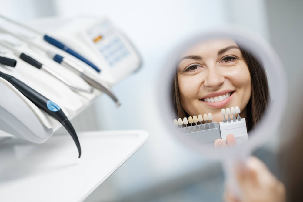 Cheerful young girl in dental clinic looking at reflection of her smile in the mirror