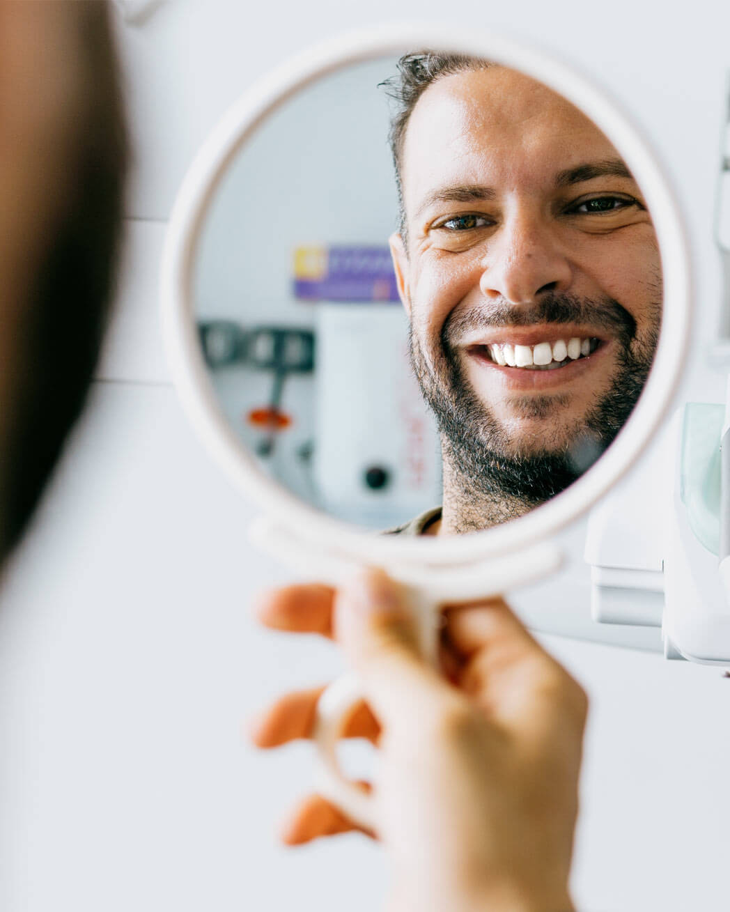 Satisfied man looks in the mirror and smiles after treatment at the dentist