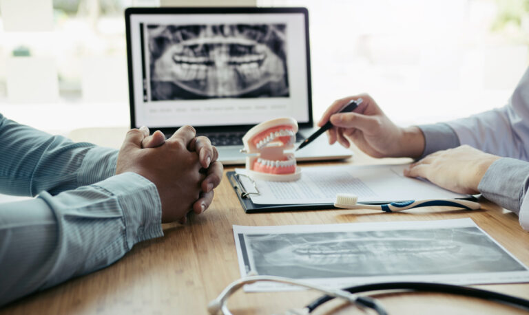 Dentists are discussing dental problems at report x-ray image on laptop screen to patients.