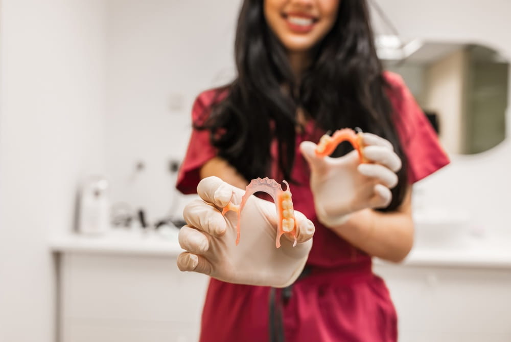 Dentist wearing gloves holding out partial dentures, illustrating options for prosthetics in a modern dental office
