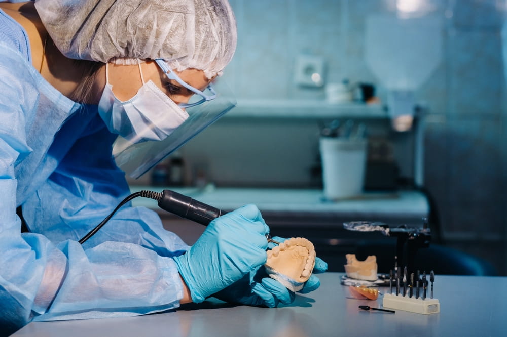 A dental technician in protective clothing is working on a prosthetic tooth in his laboratory.