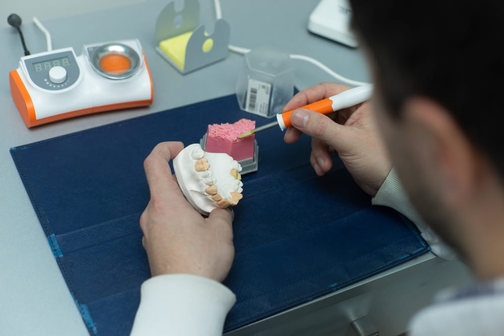 Dental technician working in a lab, crafting dental prosthetics with precision tools.