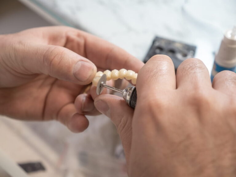 Dental technician polishing ceramic dental bridge using rotary tool in lab,