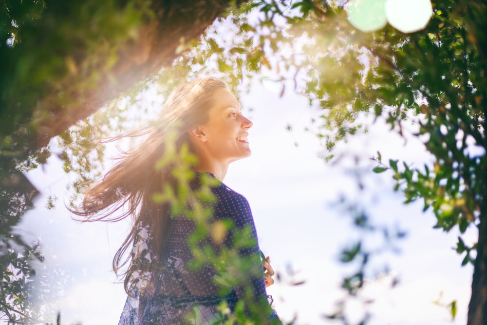 young woman in green tree branches with glare from sun