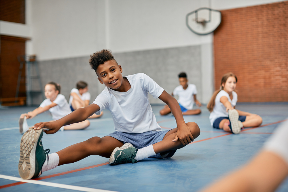 Happy elementary student stretching his leg while warming up