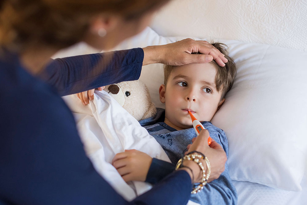 Sick boy with thermometer laying in bed and mother hand taking temperature