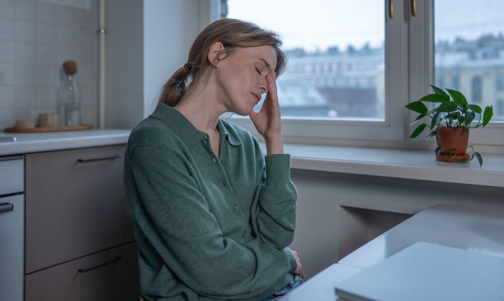 Woman seated at a table holding her head with her eyes closed