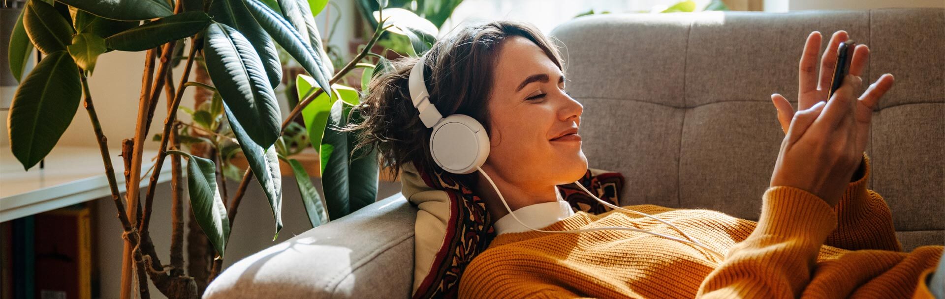 Young woman in headphones using cellphone while lying on couch