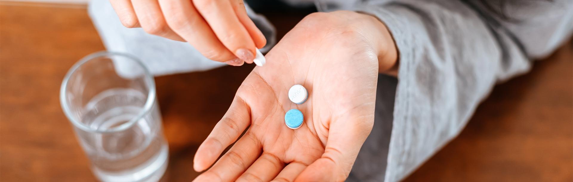 Hands with glass of water takes white round pill in hand