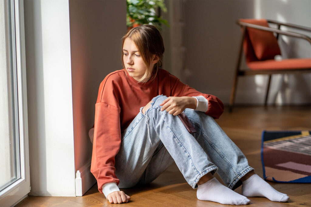 Upset teen girl sit on floor sadly look out window