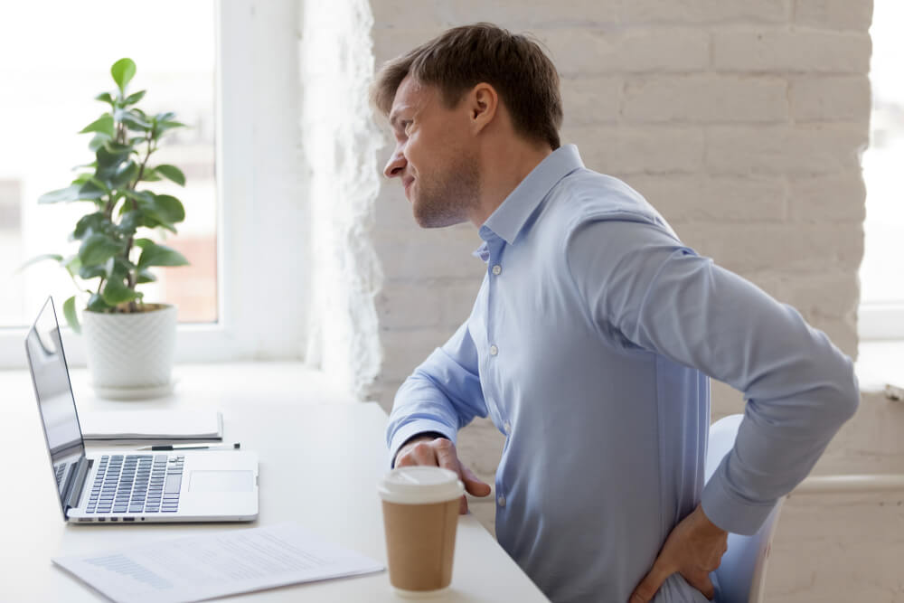 Unhealthy office worker sitting at desk opposite computer feels sudden sharp pain