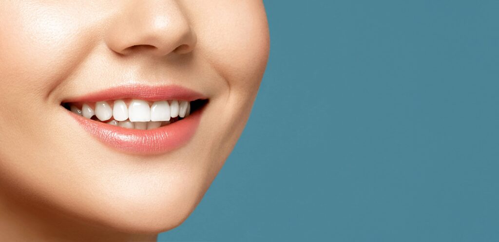 Close up portrait of a woman with healthy tooth is smiling against blue background