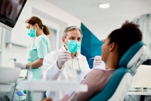 Smiling dentist communicating with African American woman while checking her teeth