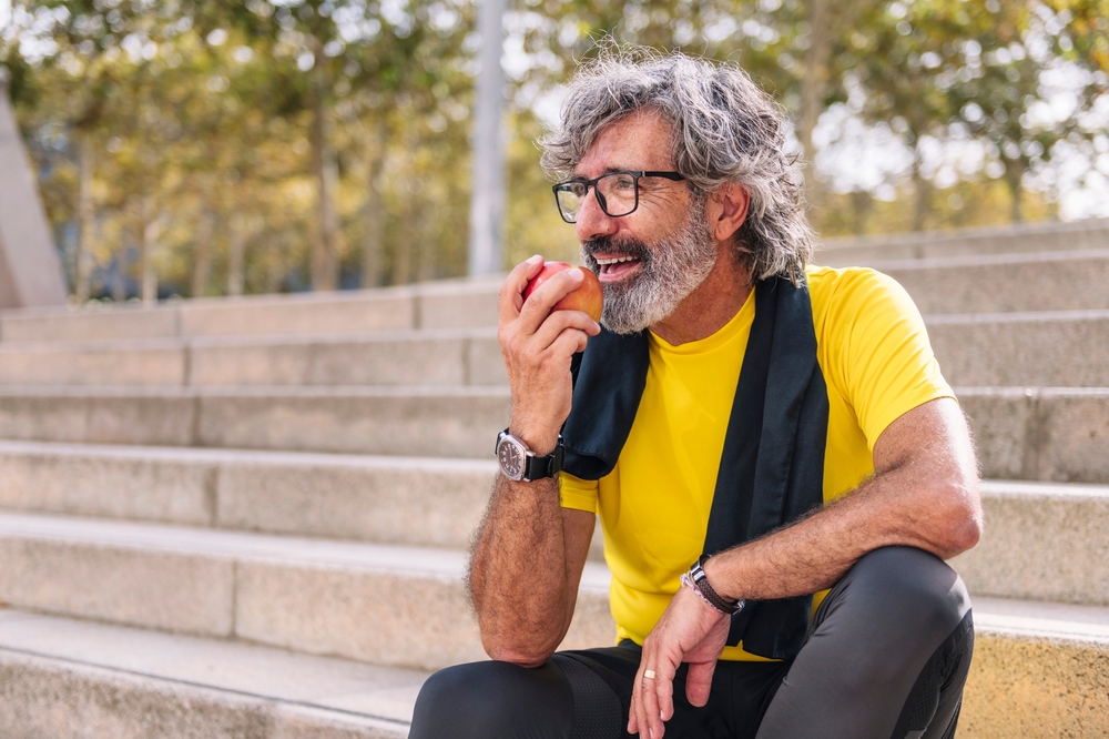 senior man rests eating an apple after workout