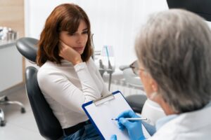 Young white brunette woman sits in the dentist's chair, holding onto her tooth in pain