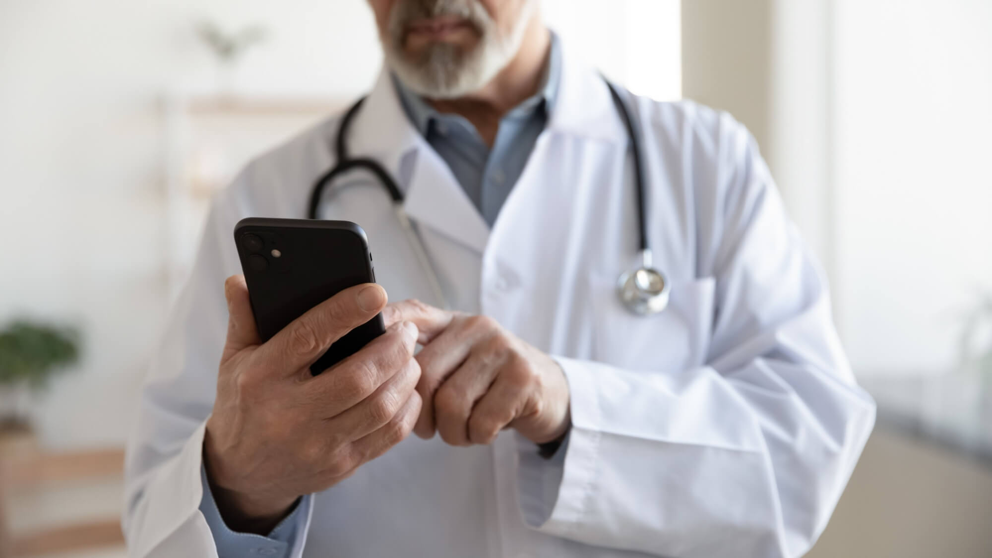 mature male doctor in white uniform hold smartphone in clinic