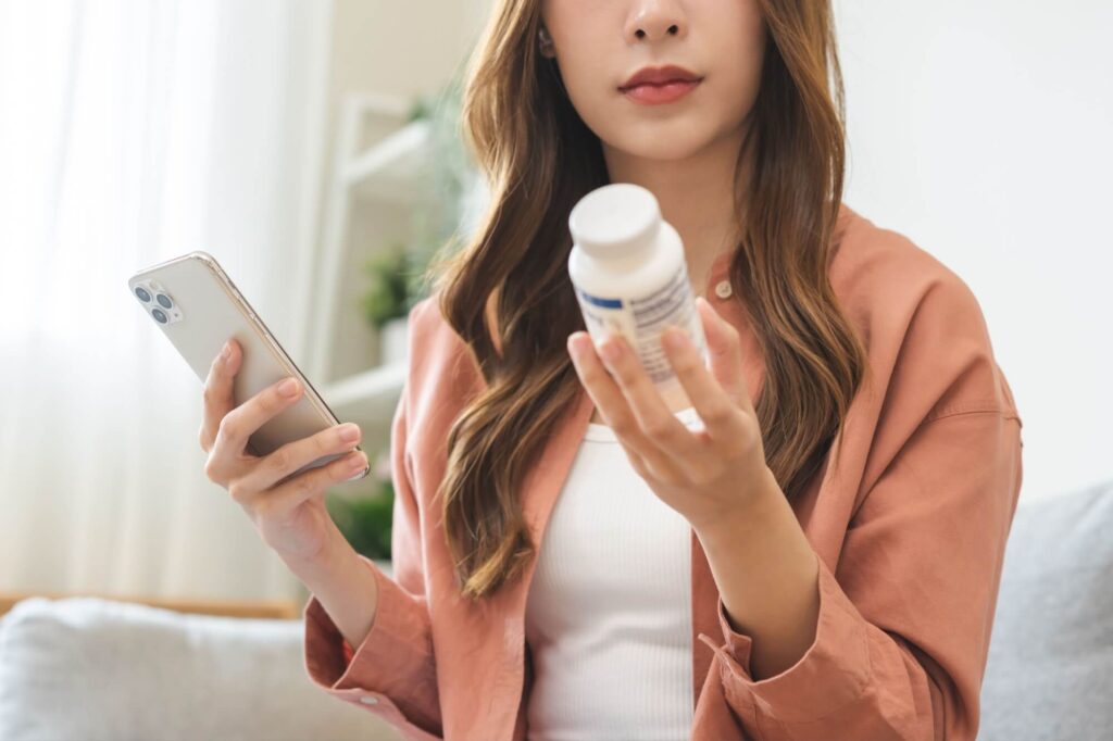 young woman using smart phone for searching prescription on medicine bottle