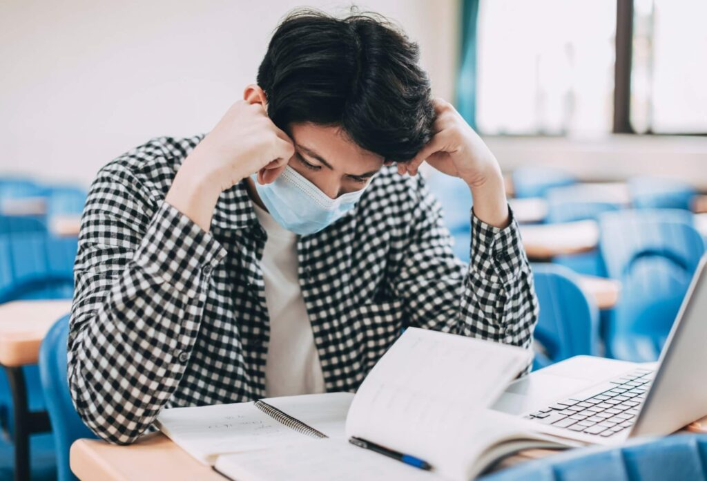 stressed young student wearing face mask and studying in classroom