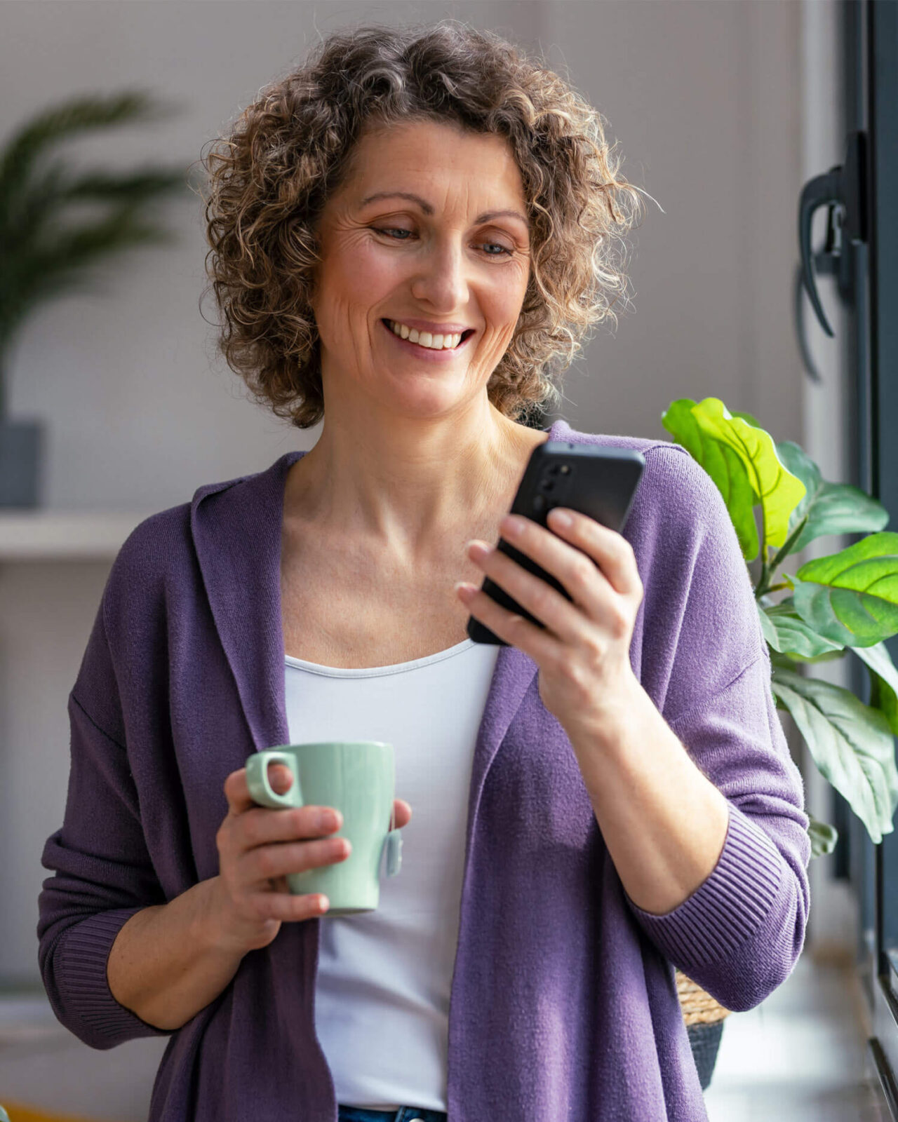 mature woman using her mobile phone while drinking coffee