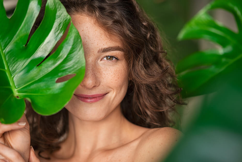 beautiful young woman covering her face by green monstera leaf