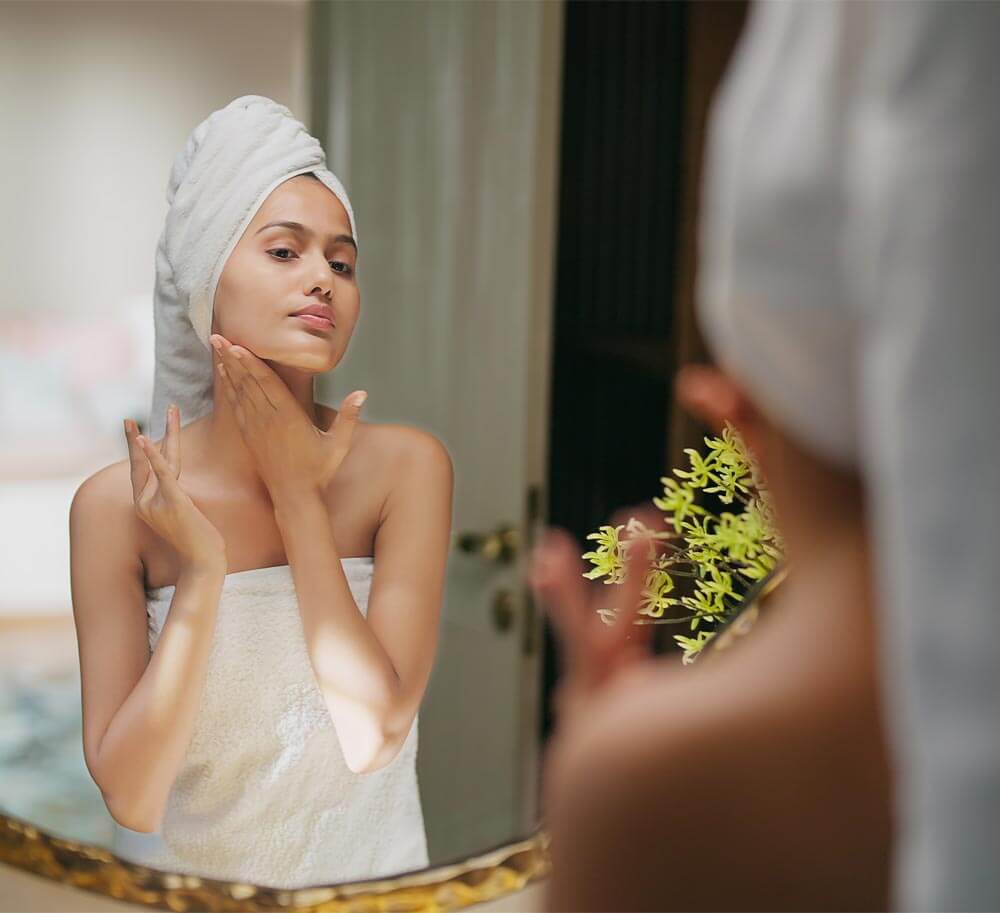 beautiful woman wrapped towel looking bathroom mirror applying cosmetics product