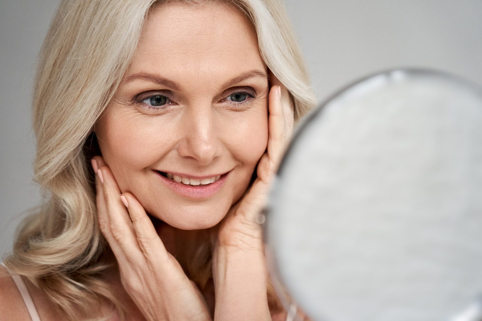 Middle aged woman touching face skin looking in mirror