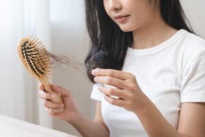 young woman holding hairbrush with fall black hair from scalp after brushing