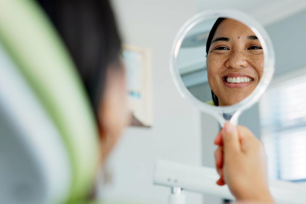 happy woman with mirror check at a dentist for teeth whitening results