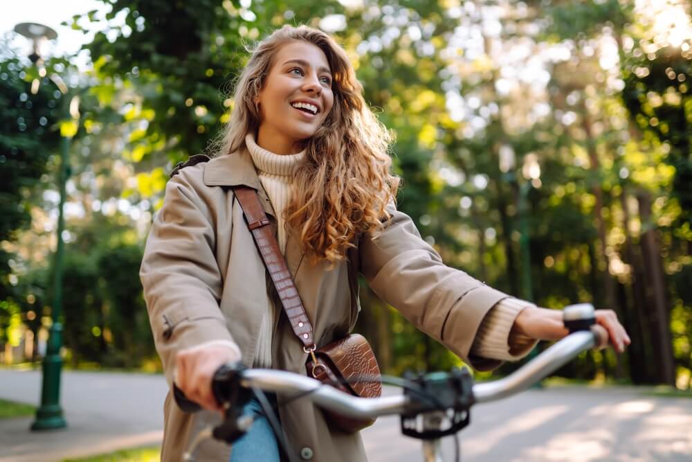 Smiling woman with curly hair in a coat rides a bicycle