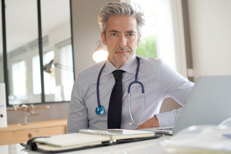 Mature doctor working in contemporary clinic office looking at camera