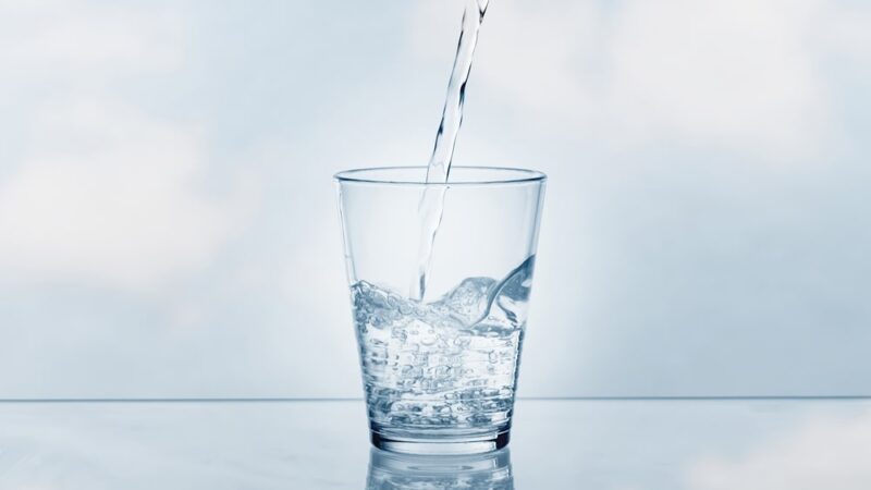 pouring drinking water in a transparent glass isolated on abstract background with glass table