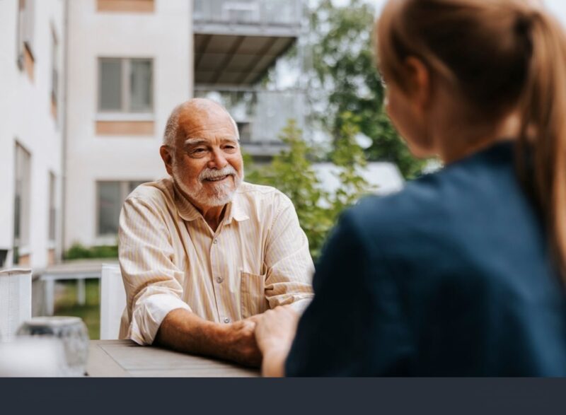 Smiling senior man holding hands of female nurse while sitting in back yard