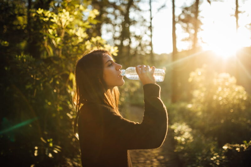 Young woman drinking water from bottle in nature.Bottled water