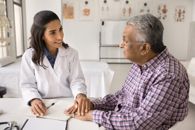 Smiling compassionate female doctor therapist surgeon comfort senior age male patient on appointment in clinic