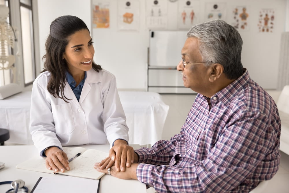 Smiling compassionate female doctor therapist surgeon comfort senior age male patient on appointment in clinic
