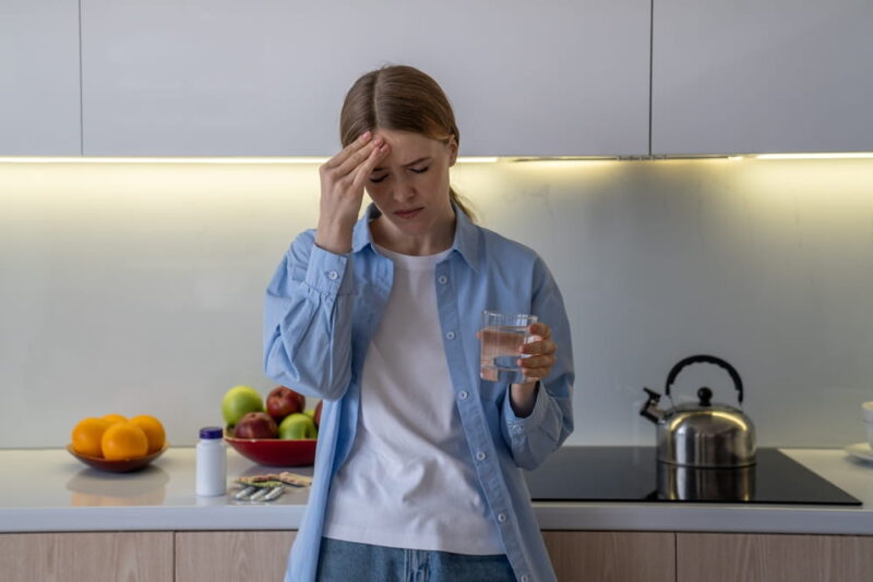 Melancholic woman swallows pills to ease headache, battling with sickness, hangover aftermath