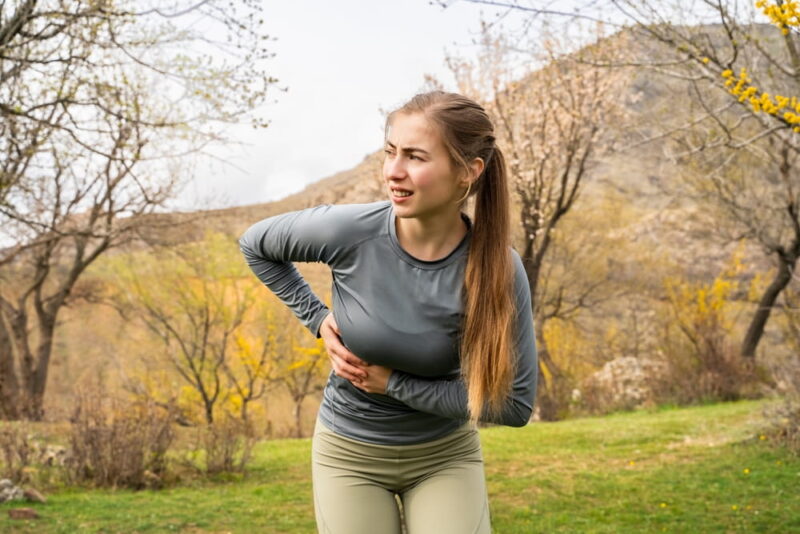 Young athletic woman in activewear holding side in pain after running outdoors
