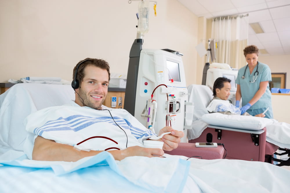 Portrait of young male dialysis patient holding glass of crushed ice during renal dialysis at hospital