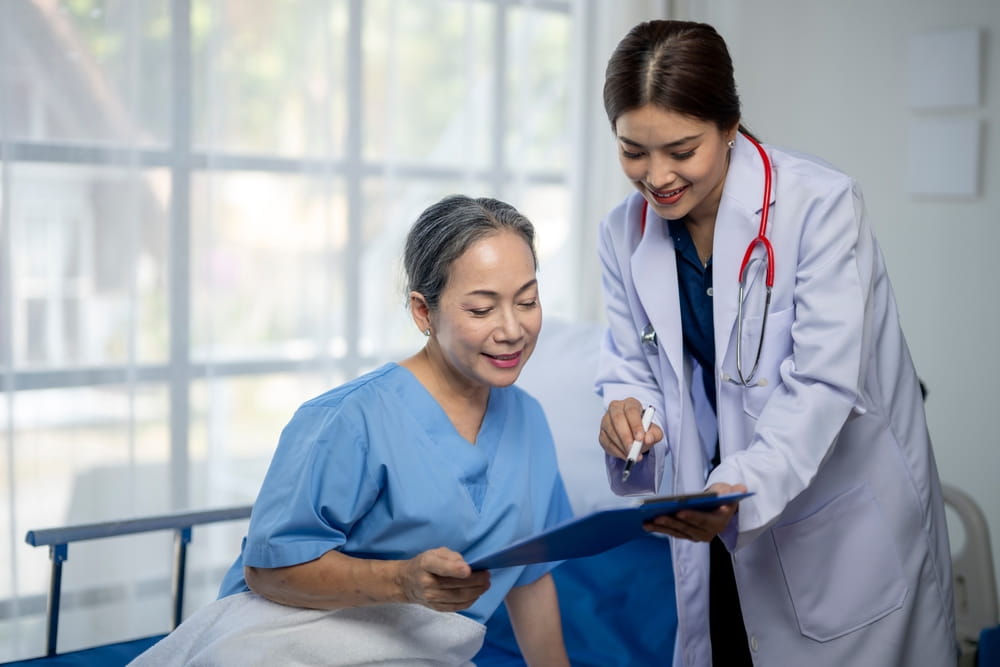 A woman in a hospital bed is being examined by a doctor. The doctor is writing something on a clipboard.