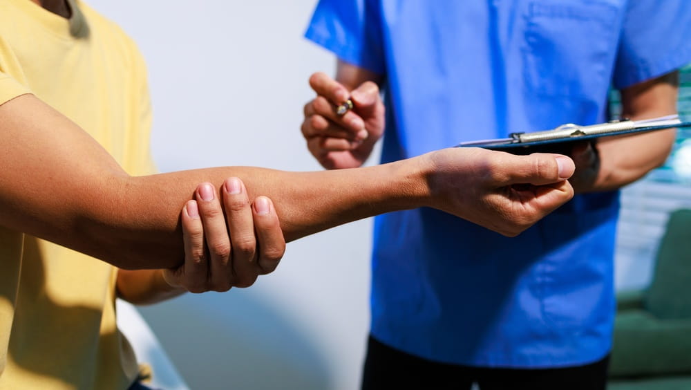 Doctor testing a patient’s arm reflex with a hammer during a physical exam in a clinic, close-up view showing healthcare assessment, diagnosis, and medical care.