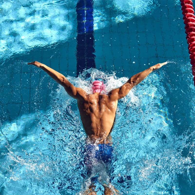 Muscular man glistening under sun swimming between red lane dividers
