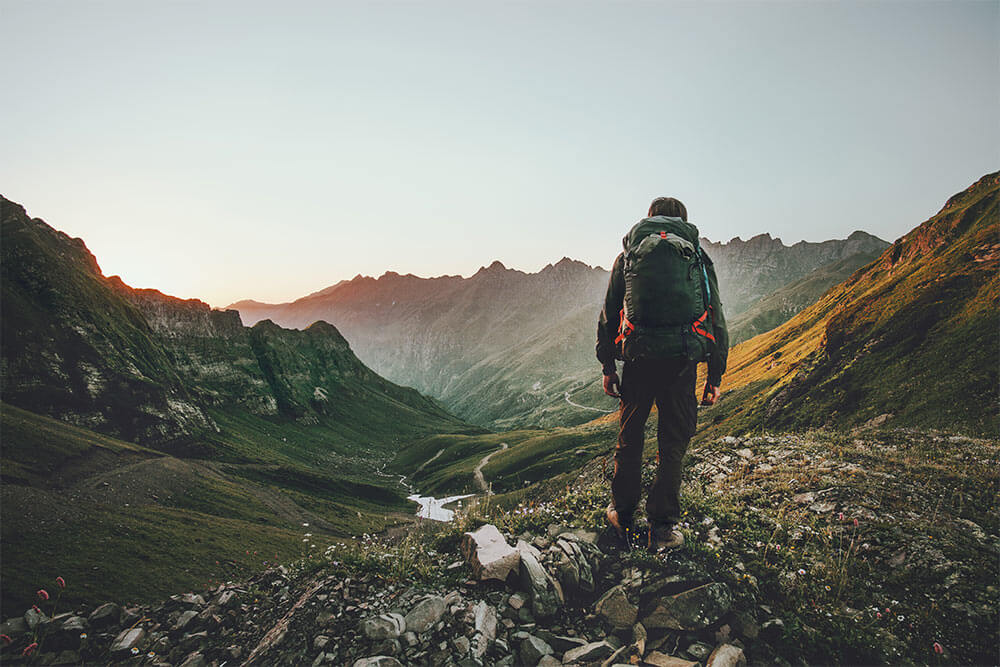 Man hiking at sunset mountains with heavy backpack