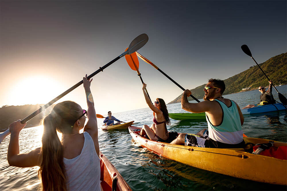 group of happy young friends are having fun and kayaking at sunset sea