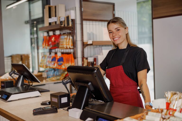 A warm and friendly barista, confidently standing at the bustling cafe counter, surrounded by fresh snacks and drinks