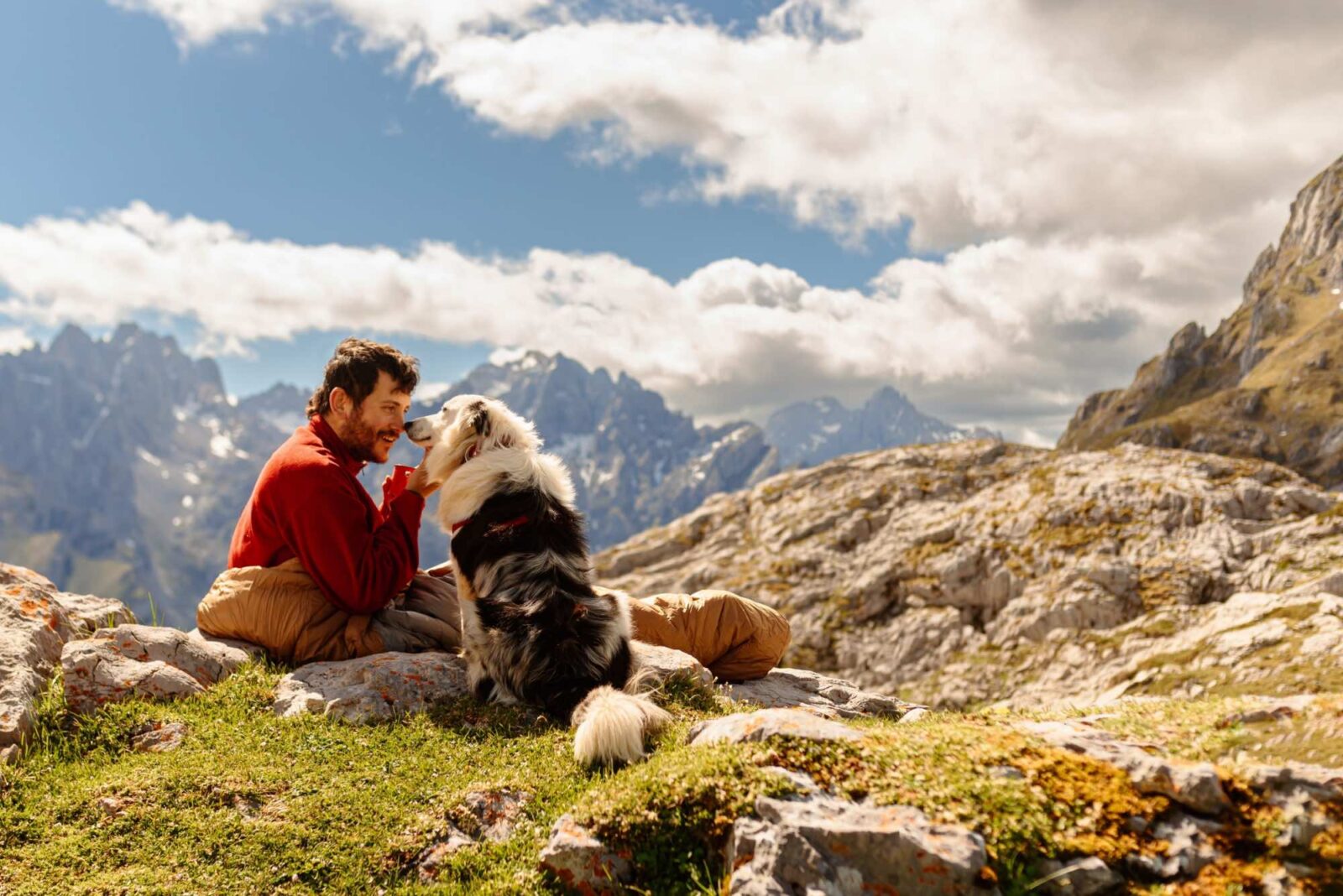 Bearded white man, mountaineer, having coffee in the mountains with his border collie dog.