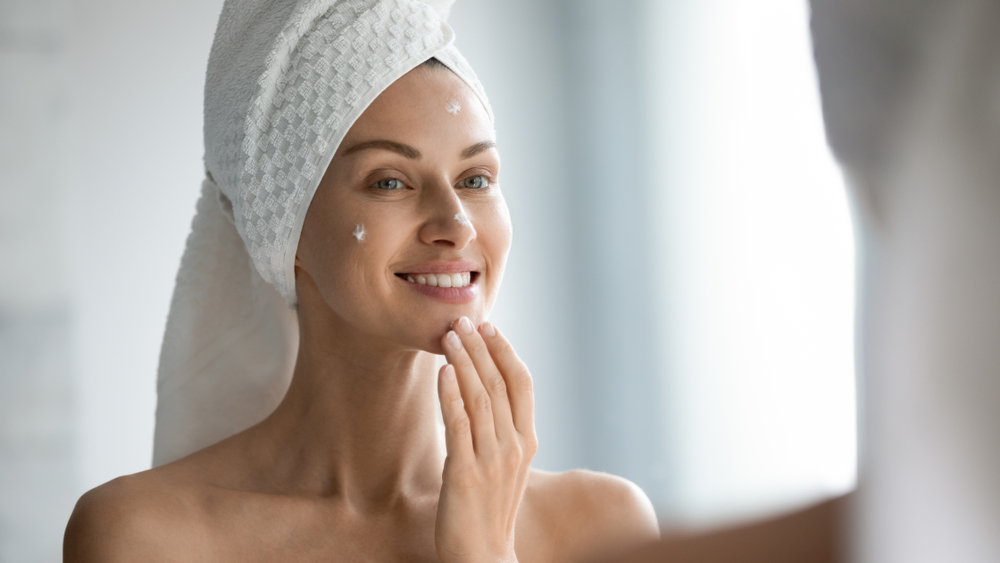 smiling, beautiful woman applies skincare cream to her face