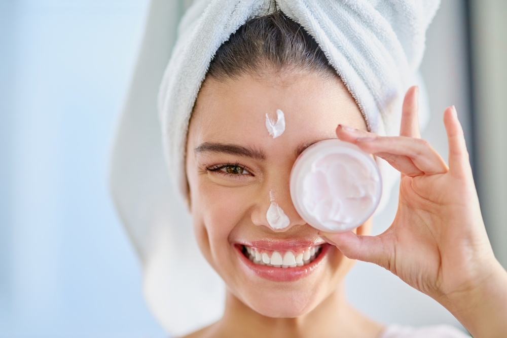 beautiful young woman applying moisturizer to her skin in the bathroom