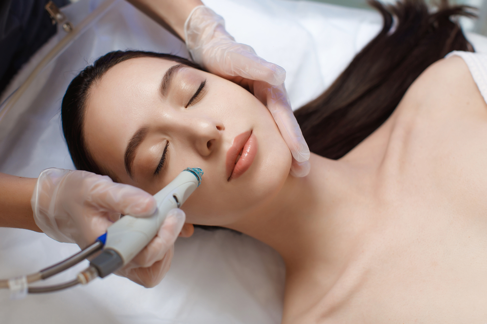 A professional female cosmetologist performs a HydraFacial in a cosmetology clinic